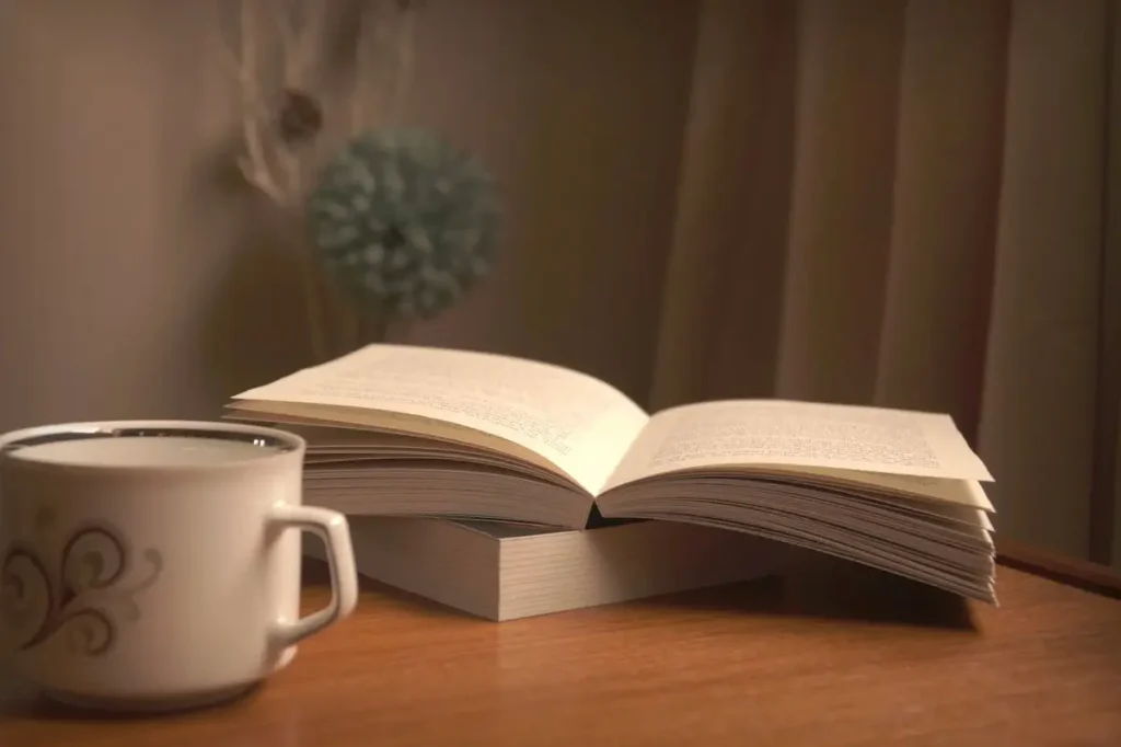 كتاب مفتوح بجانب كوب قهوة على طاولة خشبية بإضاءة دافئة